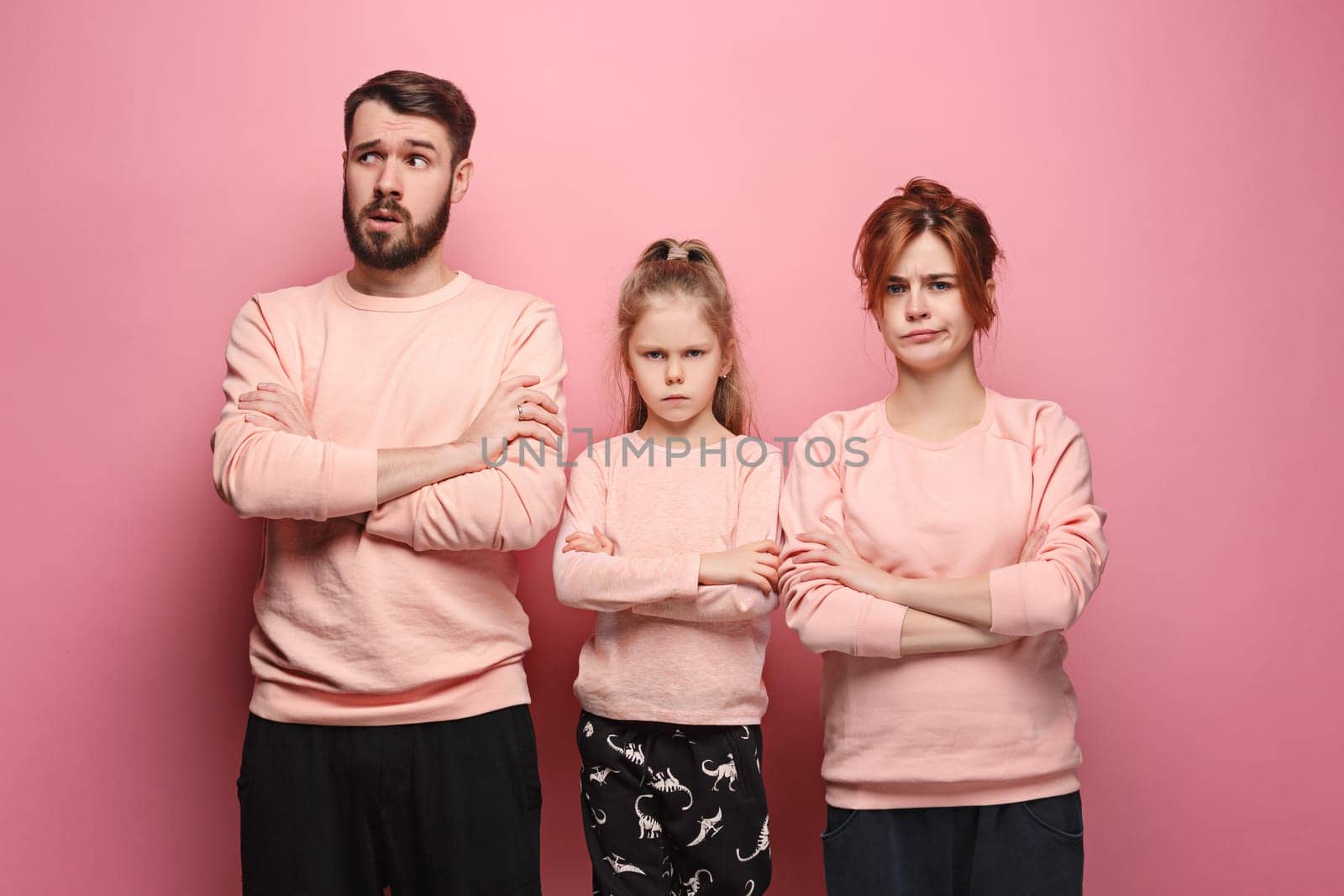 The sad and serious young family on pink studio background