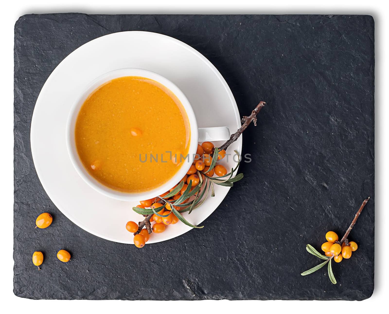 Tea of sea-buckthorn on a black slate stone. A branch of sea-buckthorn. White cup is a top view. Isolated on white background.