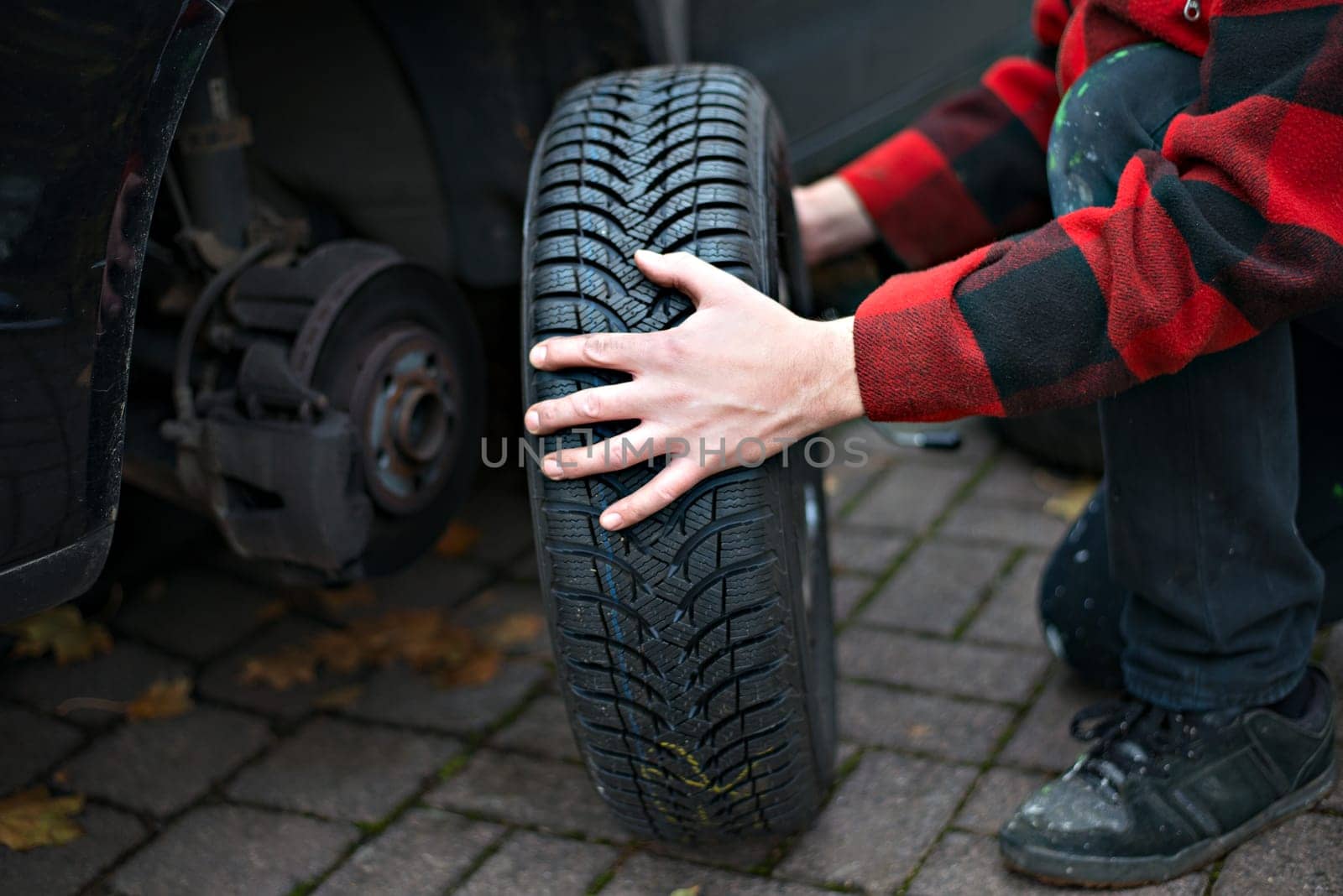 man in chequered jacket changing tyre on his car