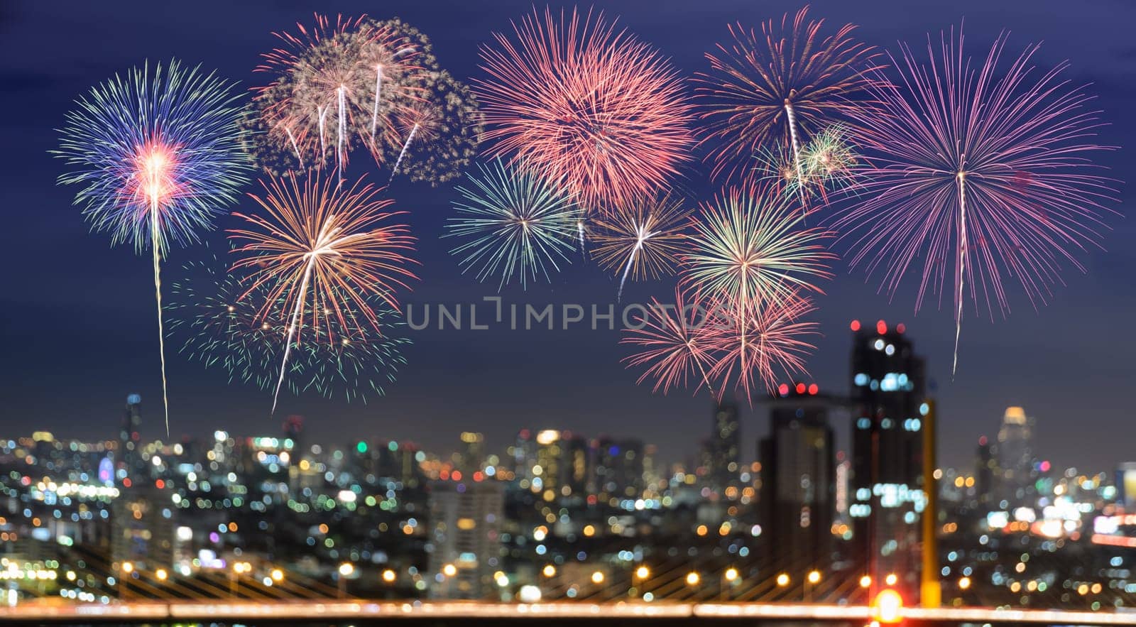 Colorful fireworks on blurred skyscrapers with city bokeh lights illuminated at night. Abstract New Year holiday or party background
