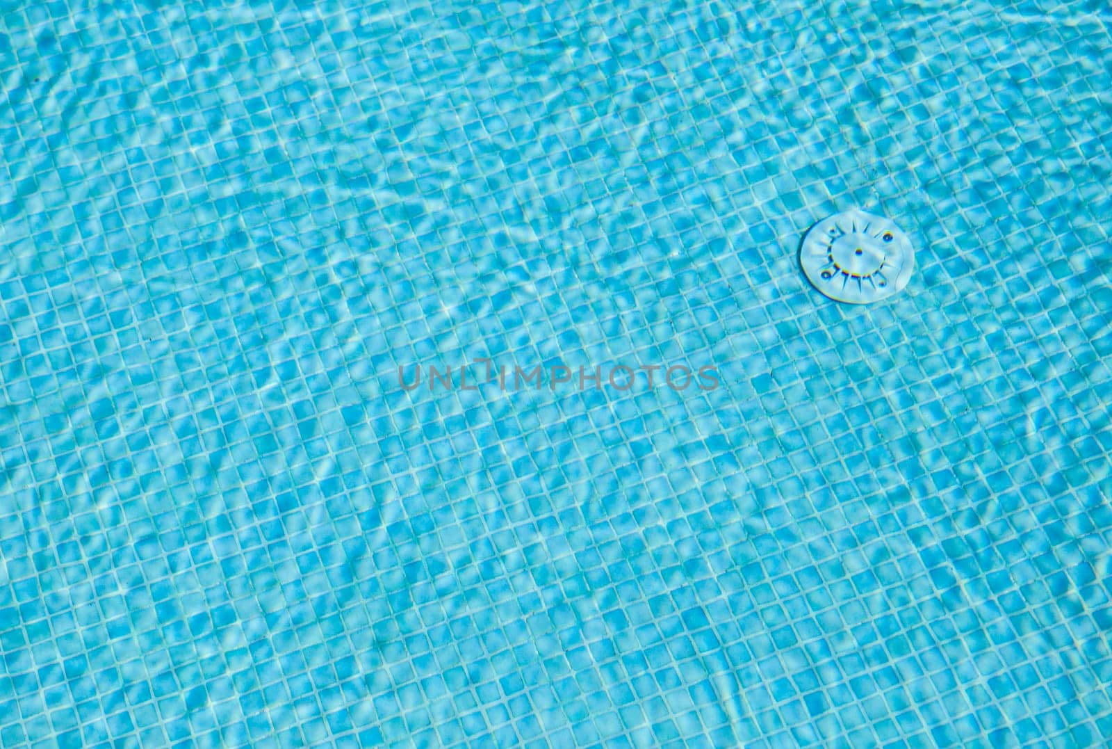 Water surface of a swimming pool with its bottom with a drain over patterns mosaic tile background