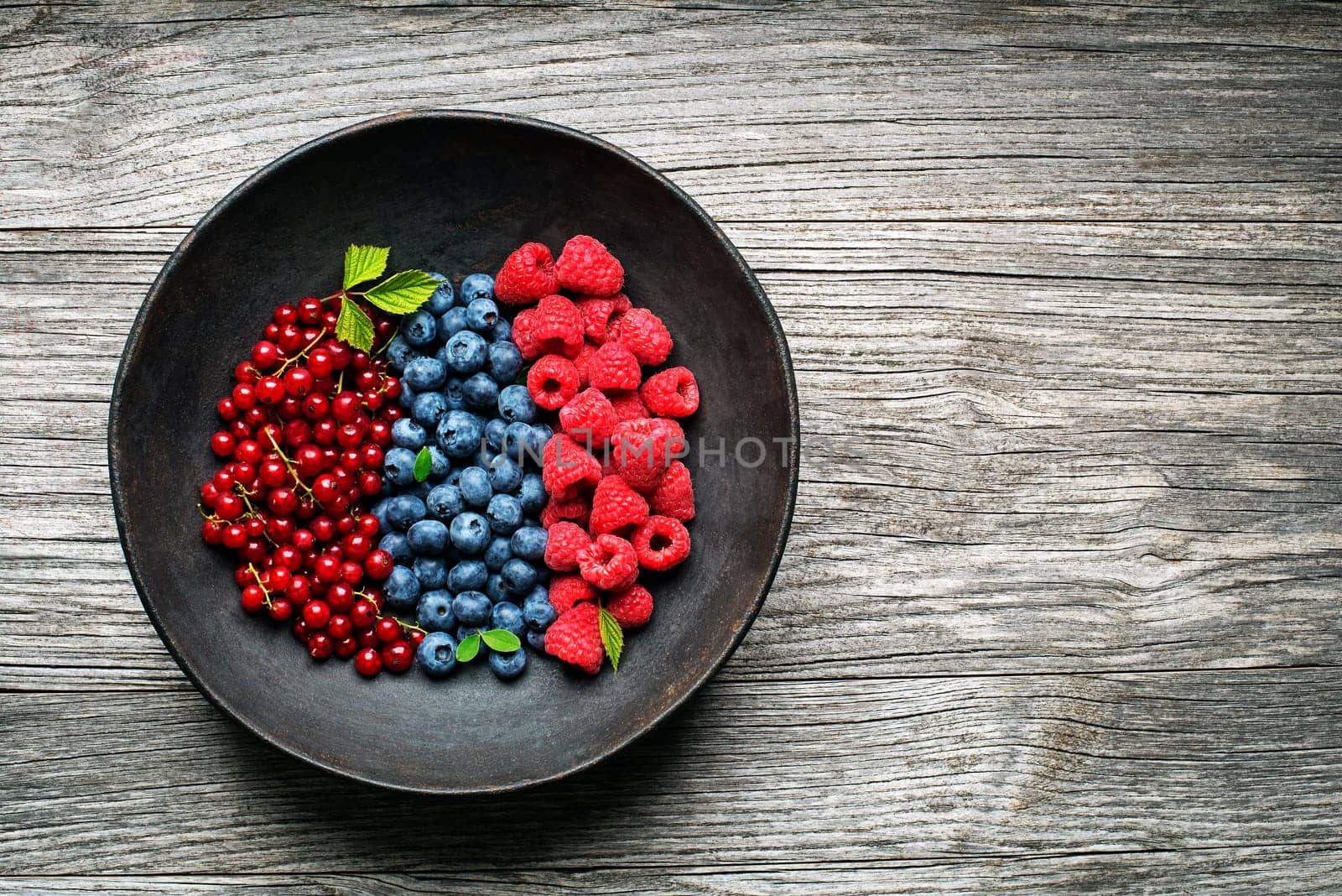 Mix of fresh berries in a bowl on wooden background