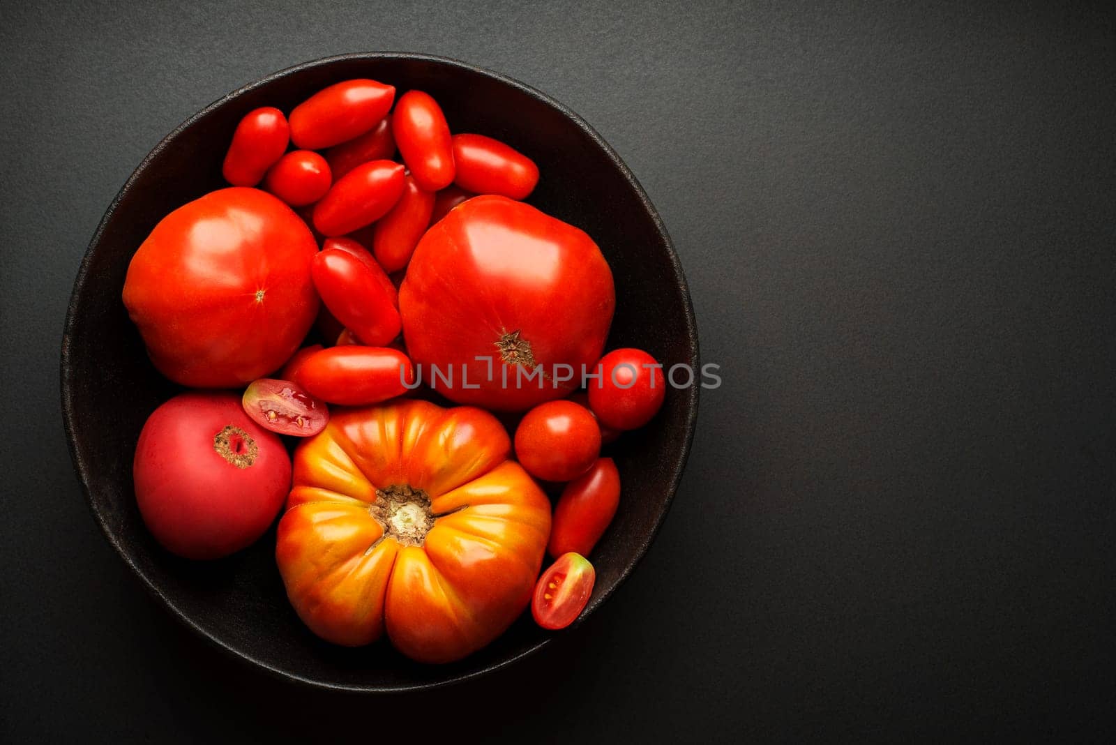 Fresh red tomatoes in a bowl on black background. Top view
