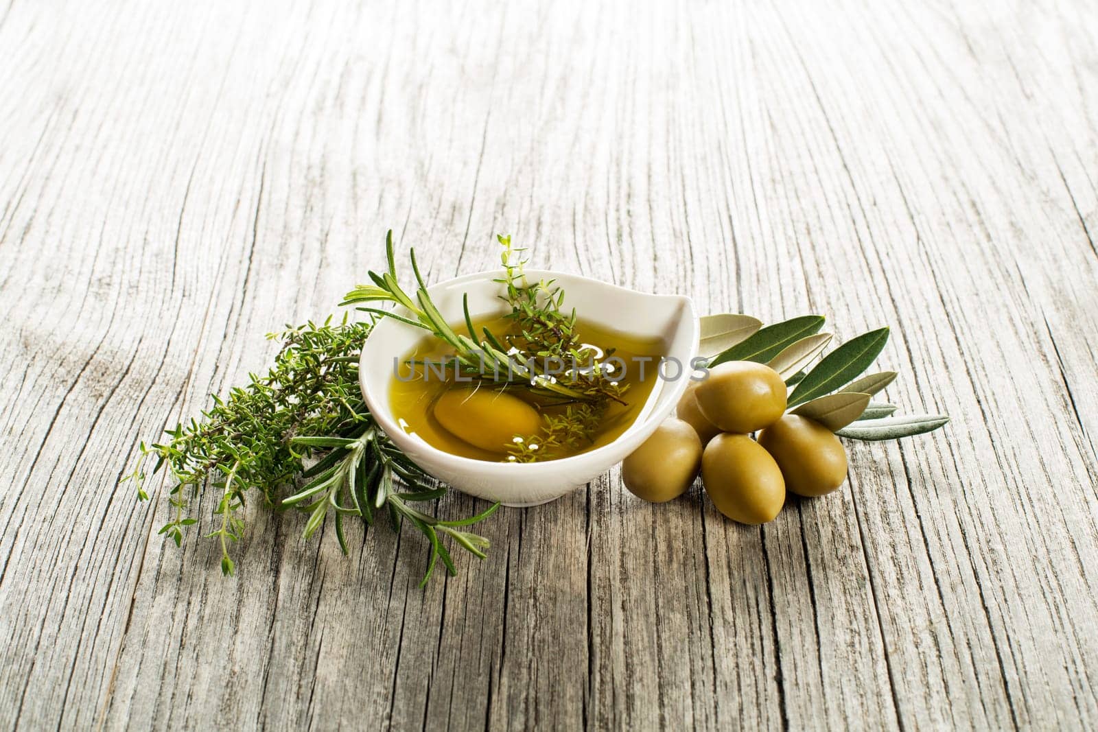 Olive oil with fresh herbs and spices on wooden background
