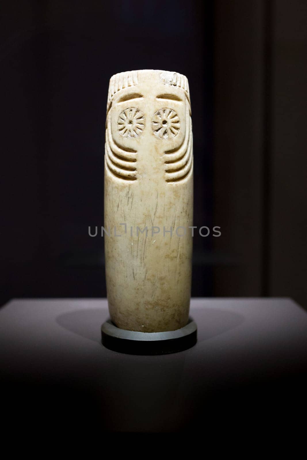 Madrid, Spain - November 10th, 2017: Cylindrical alabaster idol with face depicted. Front view. National Archeological Museum, Madrid