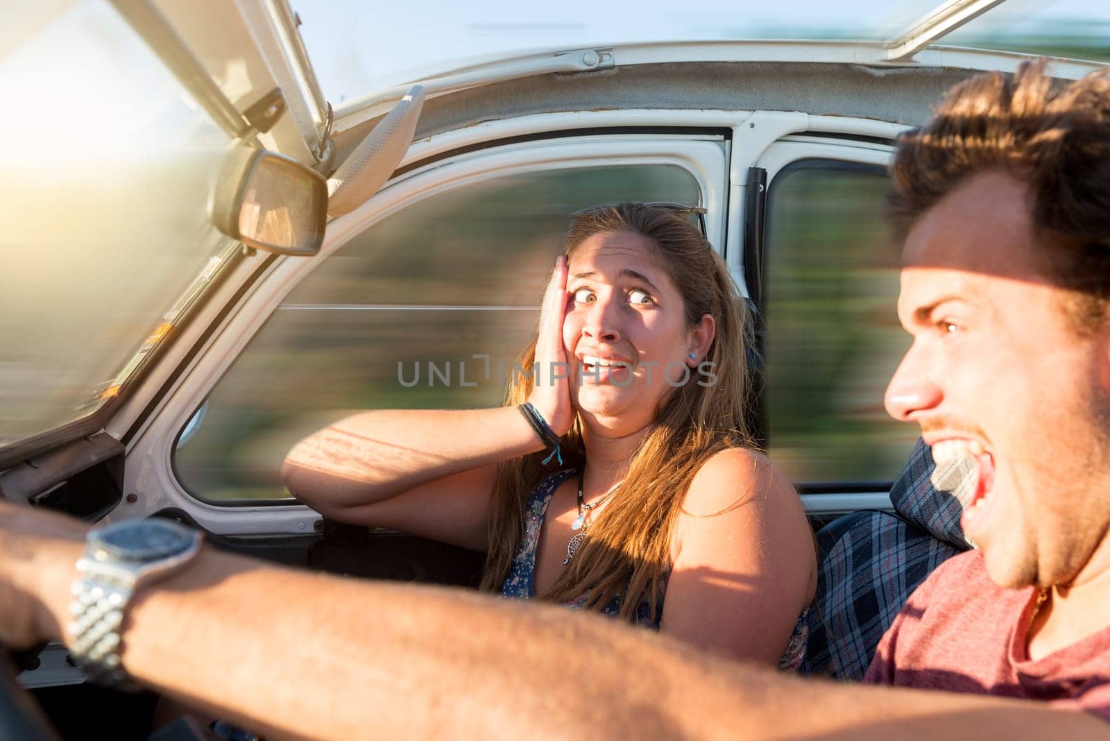 Couple in a car at sunset, with male driving fast and girl scared, screaming and praying.