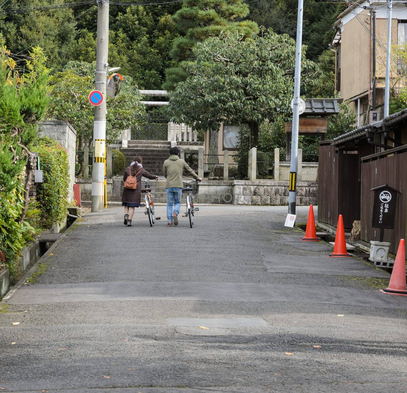 Rear view of young man and woman walking with bicycles in Kyoto, Japan