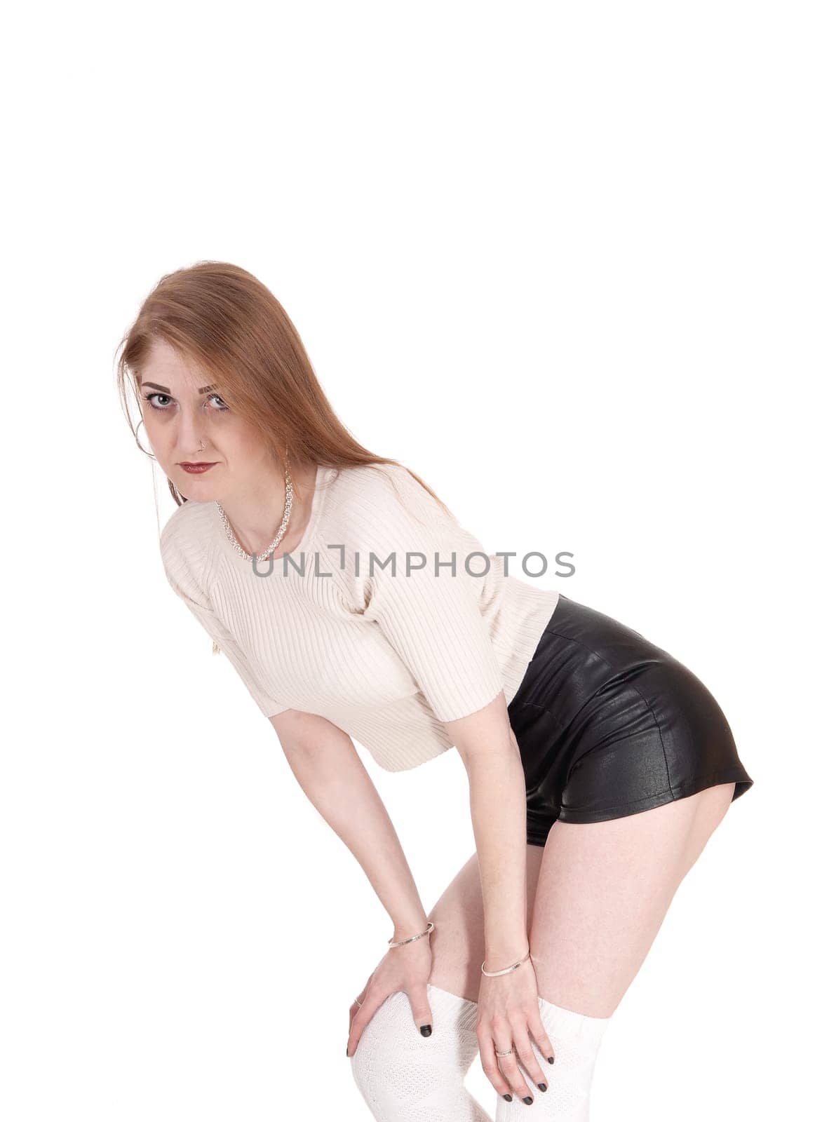 A young lovely brunette woman standing over white background in.black leather shorts and long white socks bending forwards.