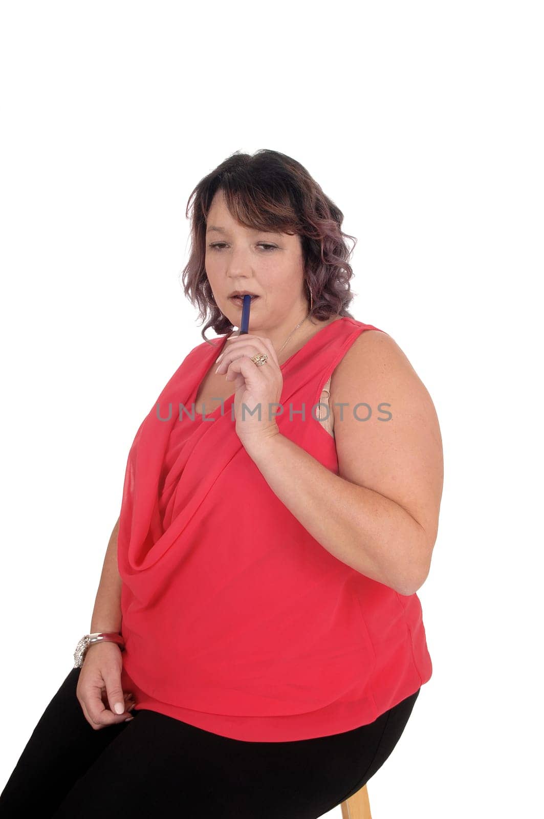 A lovely oversized woman in a red blouse sitting on a chair with her.pen in her mouth, thinking, isolated for white background.