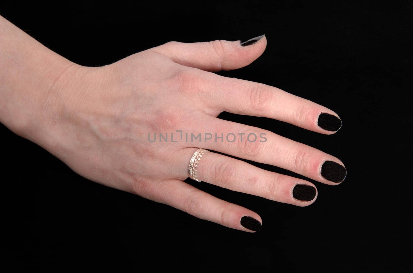 A close up image of the hand of a young woman with her black finger.nails and a ring, isolated for black background.