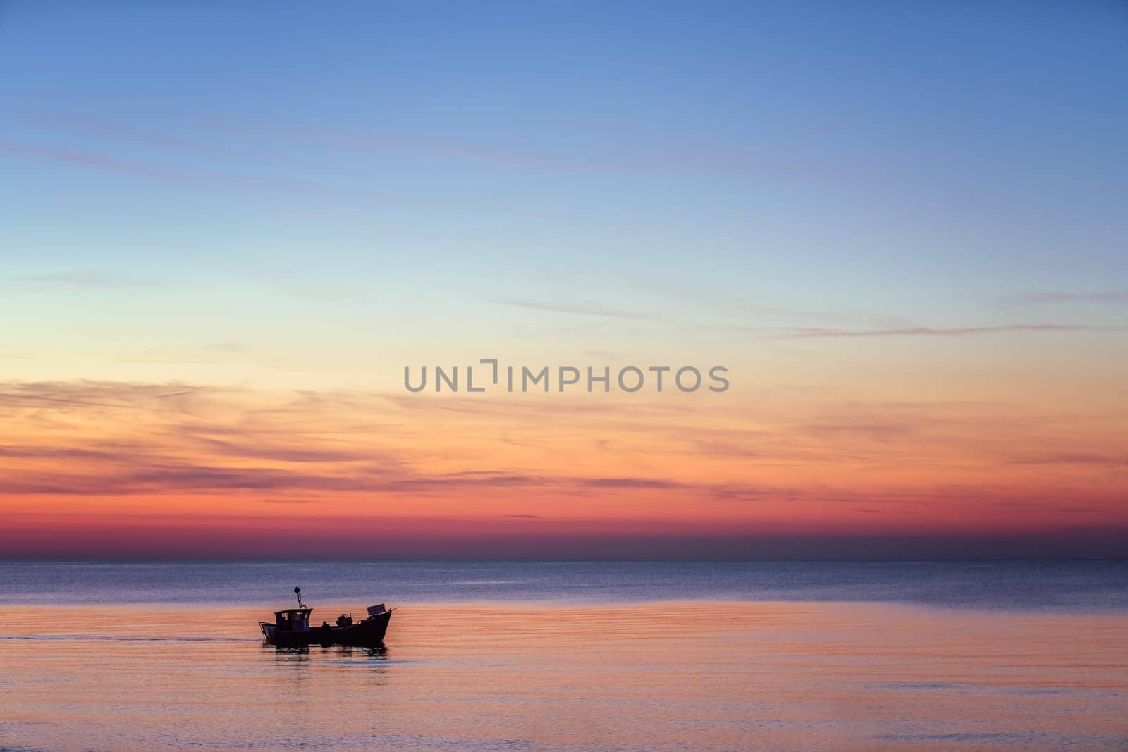 Small fisherman boat sailing at dusk on the calm sea