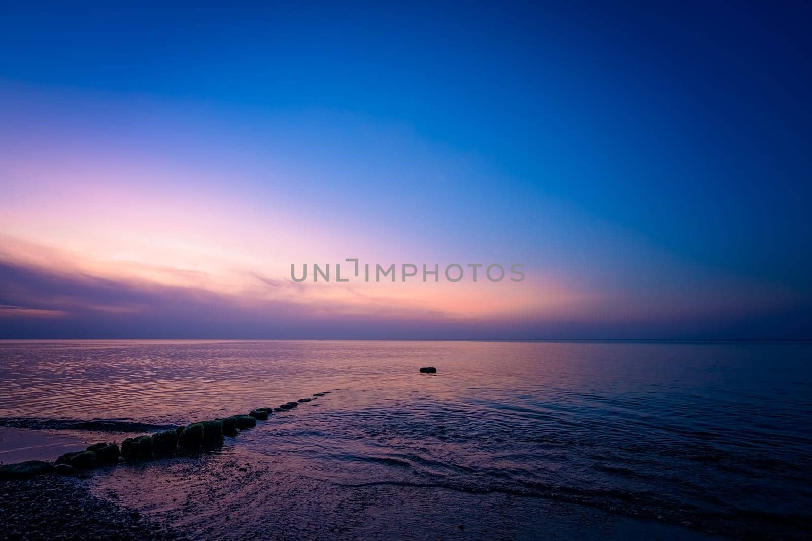 Old wooden breakwaters on the Baltic coast beach photographed after sunset
