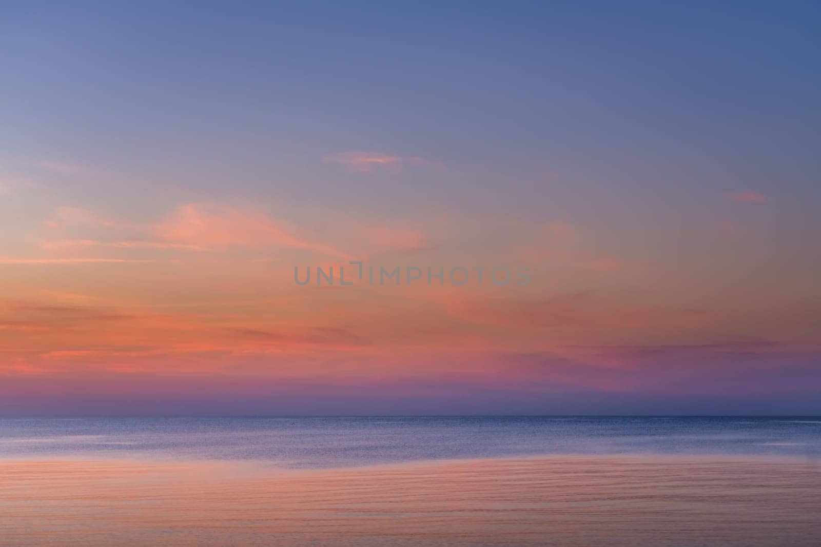 Horizontal picture of clouds in the sky above calm sea surface during sunset