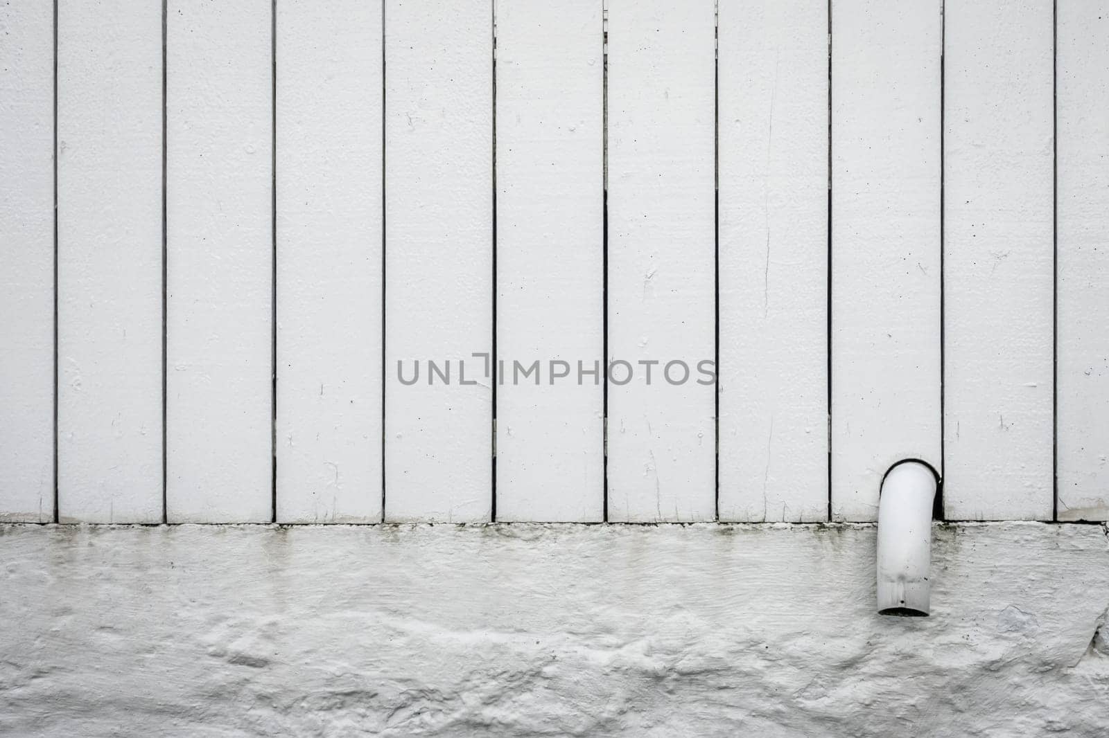 Detail of a small pipe tip sticking out of a white wooden fence
