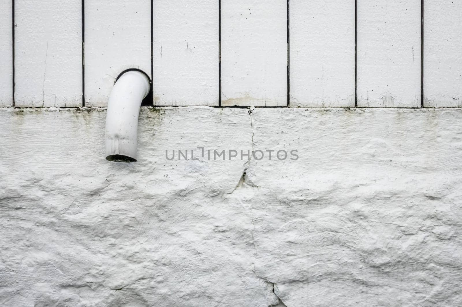 Detail of a small pipe tip sticking out of a white wooden fence