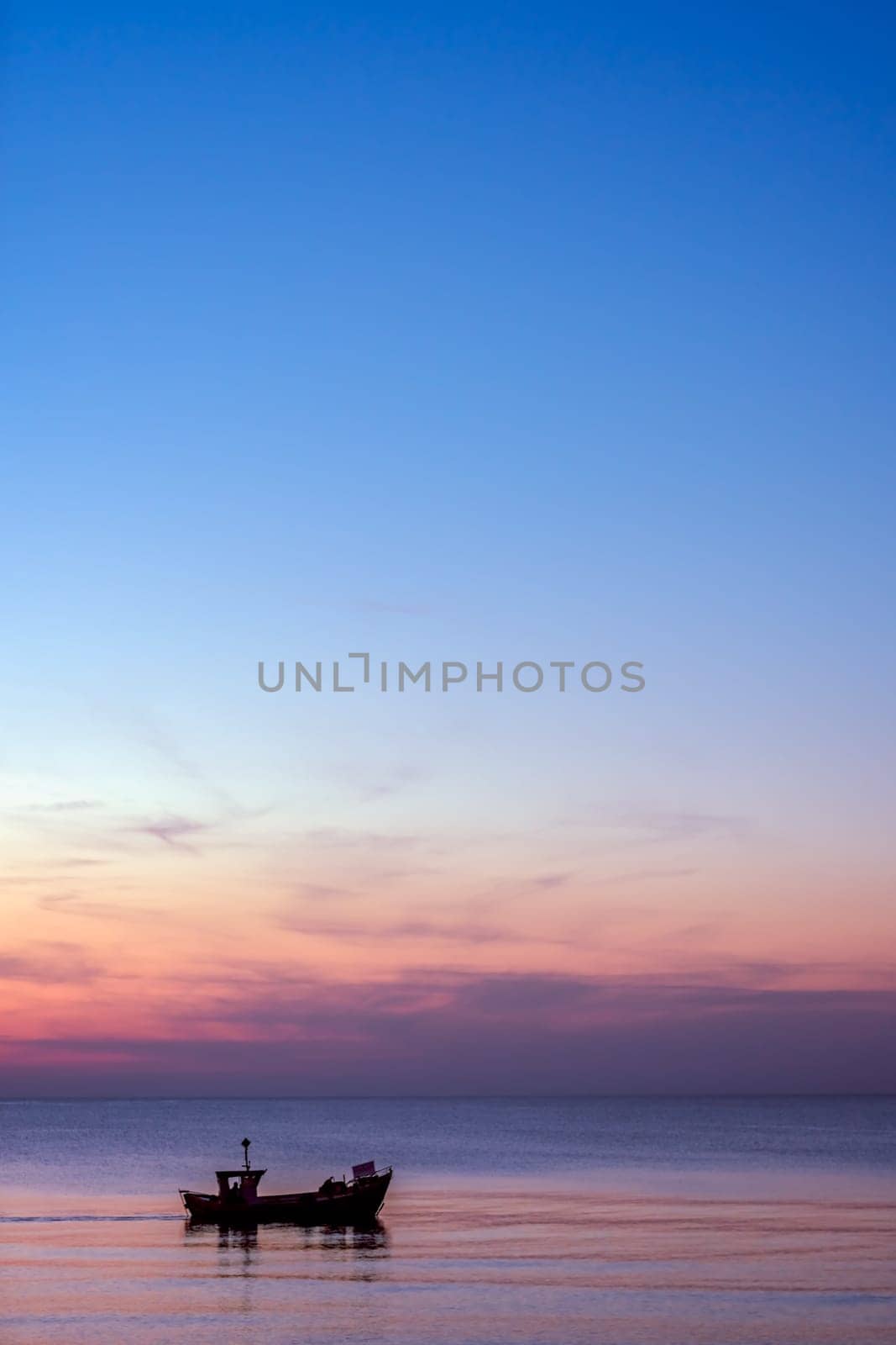 Small fisherman boat sailing at dusk on the calm sea