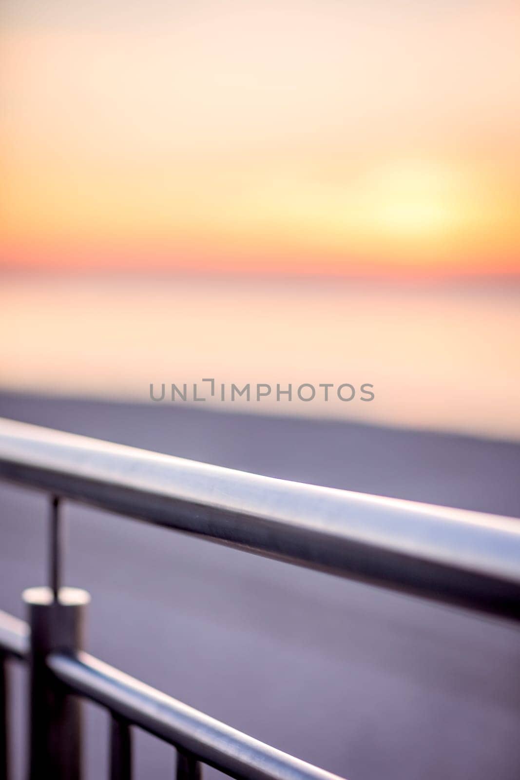 A detail of the metal iron fence of the railing on the beach promenade at sunset