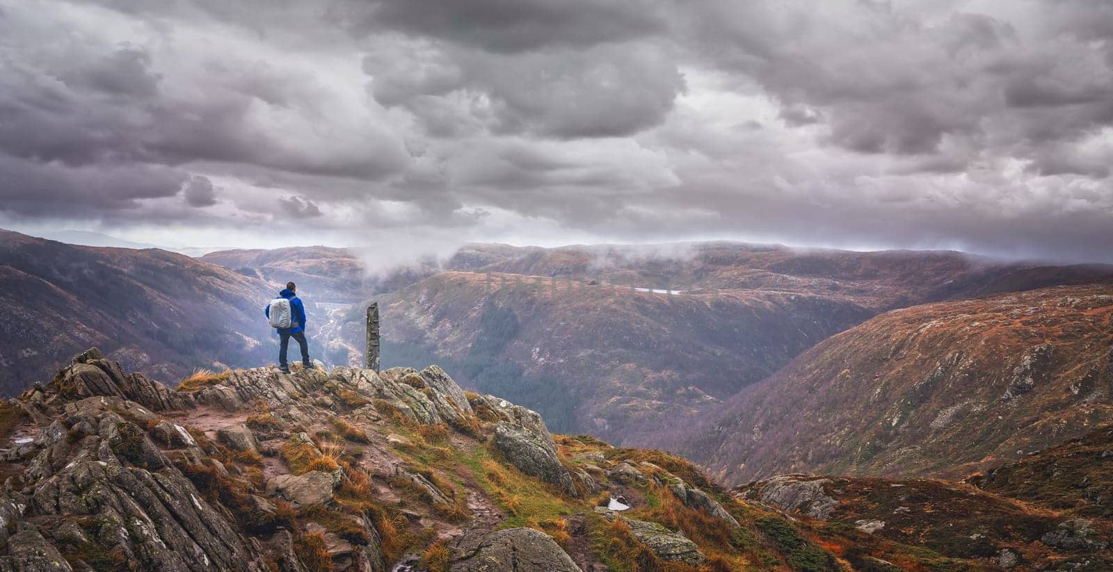 Trekker with a backpack standing on the top of mount Ulriken in Bergen and looking at the landscape below, Norway