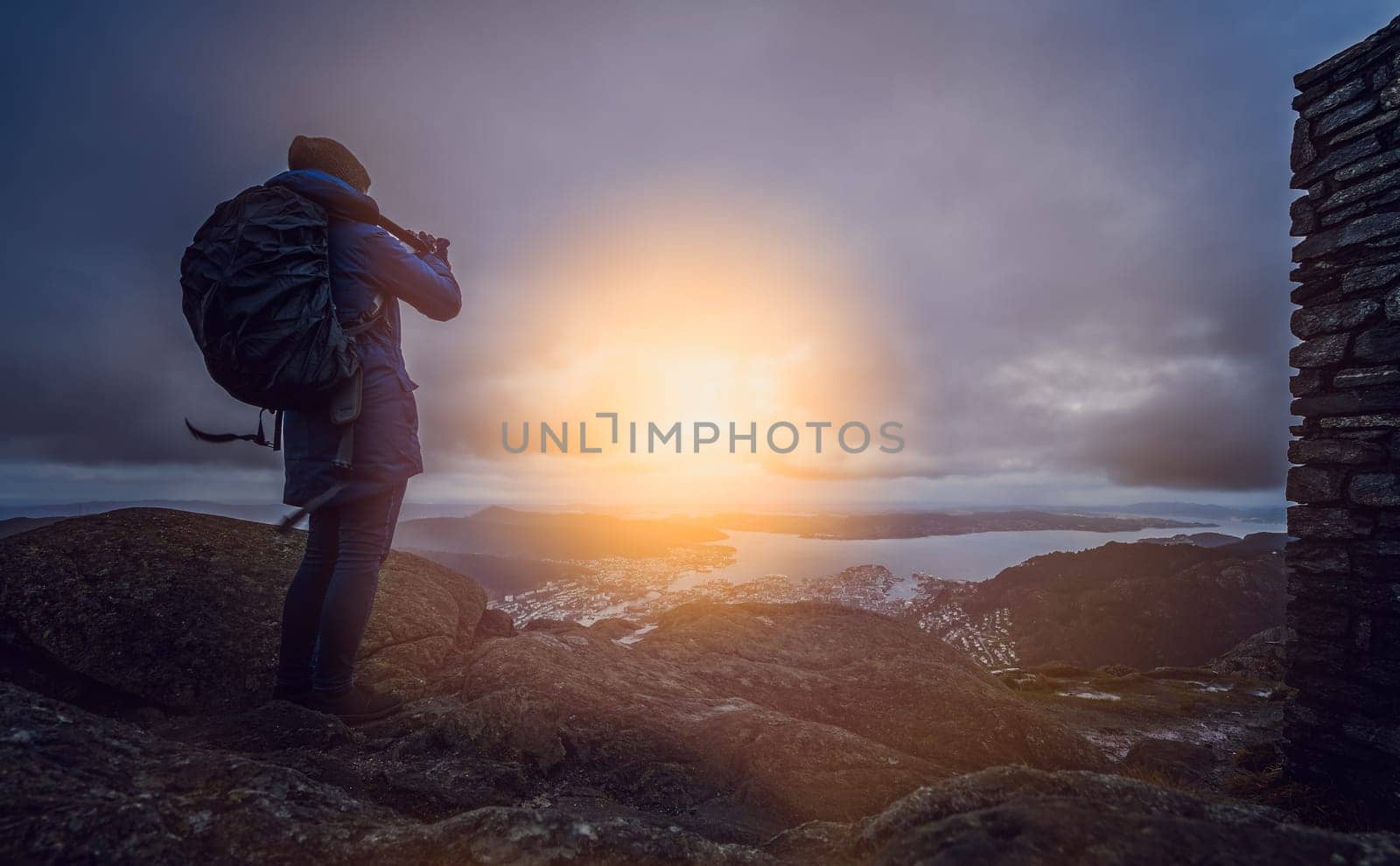 Backpacker tourist standing on the top of mount Ulriken in Bergen and taking pictures of the town and landscape below, Norway