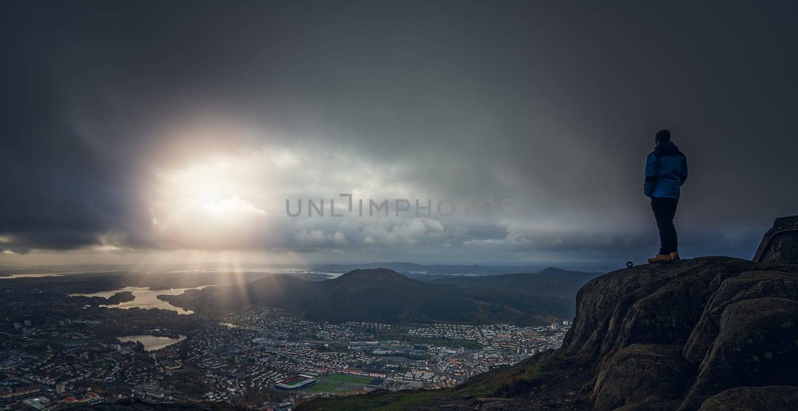 Unidentifiable tourist standing on the top of mount Ulriken in Bergen and looking at the landscape below, Norway