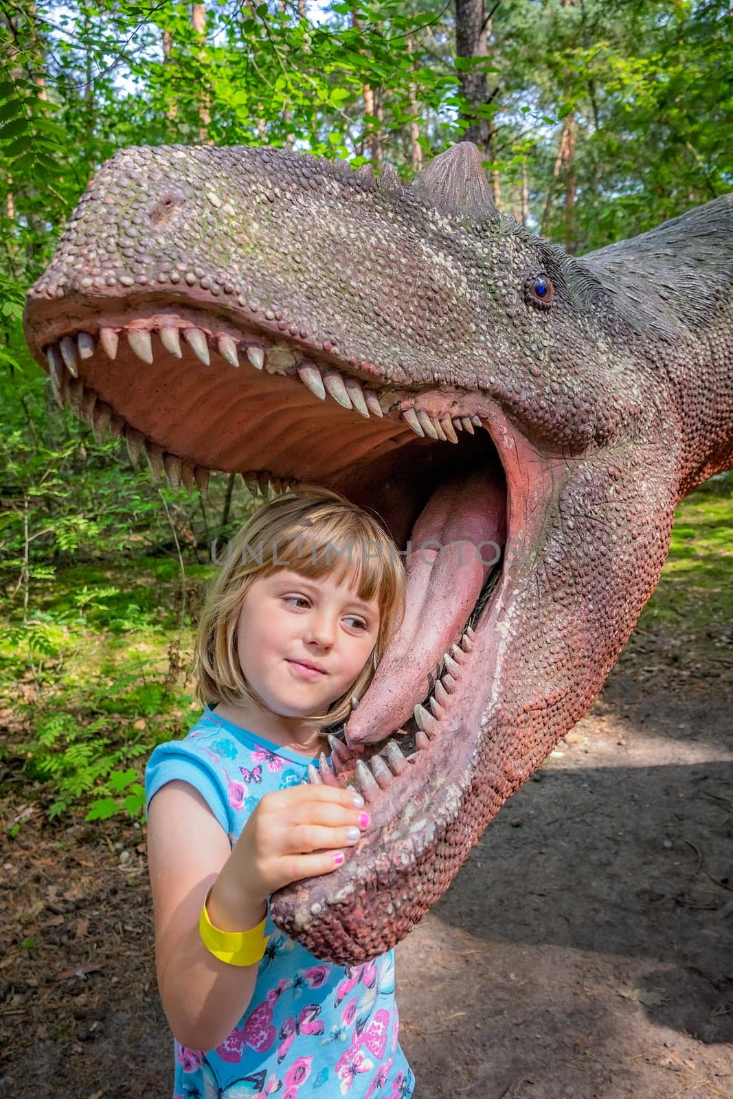 Cute little caucasian girls head in the mouth of a dinosaur replica in an amusement park