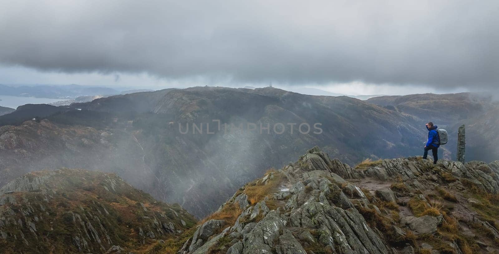 Trekker with a backpack standing on the top of mount Ulriken in Bergen and looking at the landscape below, Norway