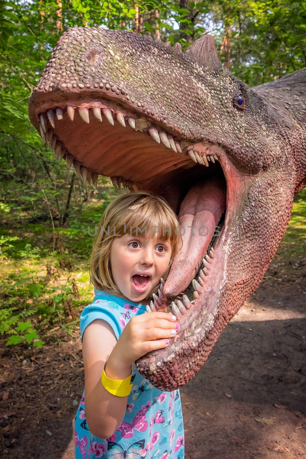 Cute little caucasian girls head in the mouth of a dinosaur replica in an amusement park
