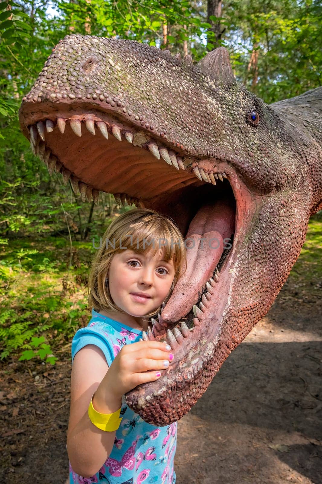 Cute little caucasian girls head in the mouth of a dinosaur replica in an amusement park