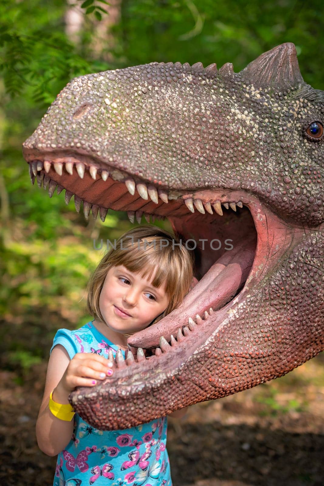 Cute little caucasian girls head in the mouth of a dinosaur replica in an amusement park