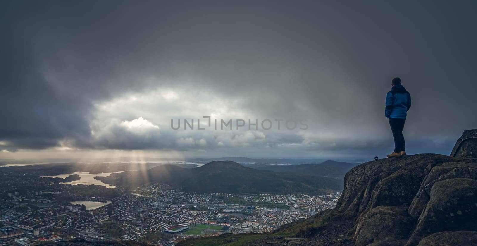 Unidentifiable tourist standing on the top of mount Ulriken in Bergen and looking at the landscape below, Norway