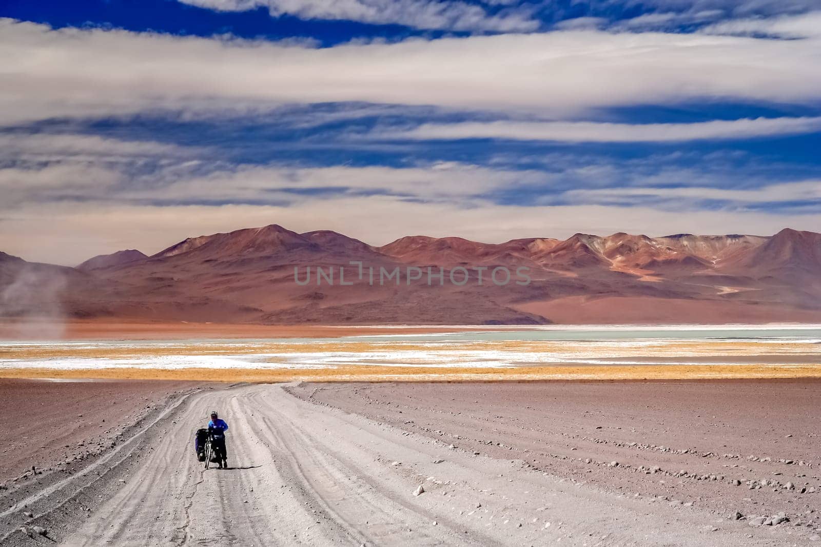 Woman cyclist struggling and pushing her bike on the sandy corrugated road in Altiplano in Bolivia