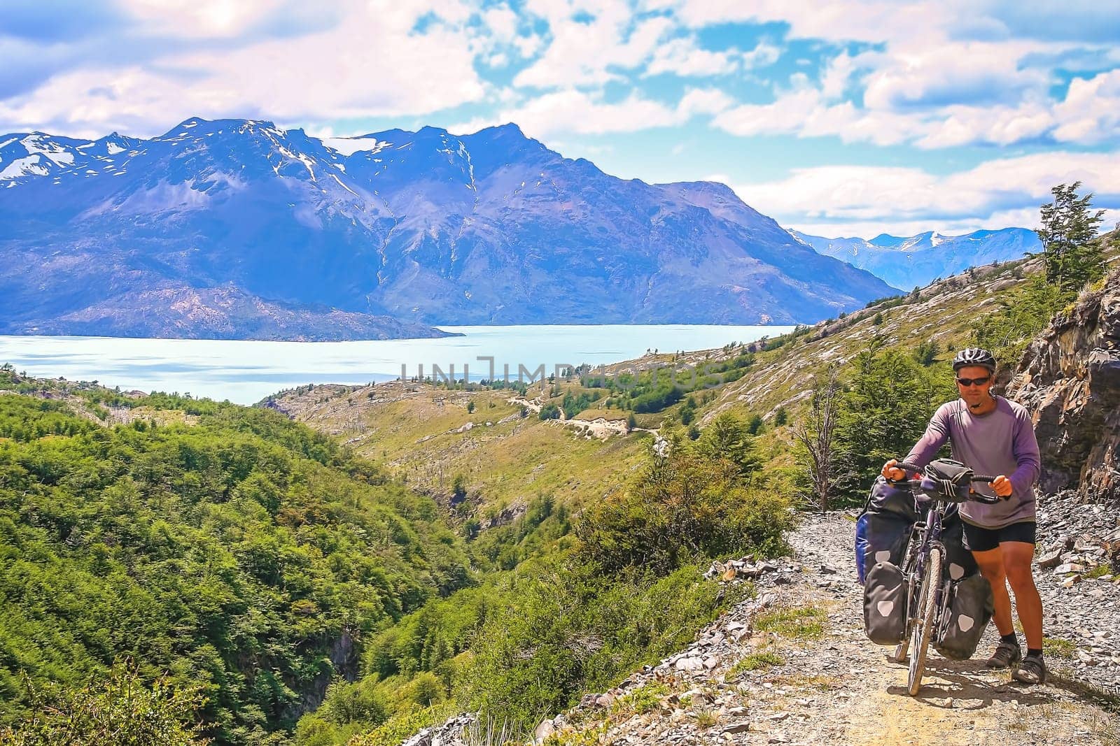 Cyclist pushing his bicycle uphill on a narrow rocky path at the end of the Carretera Austral, leading to the border between Chile and Argentina, South America