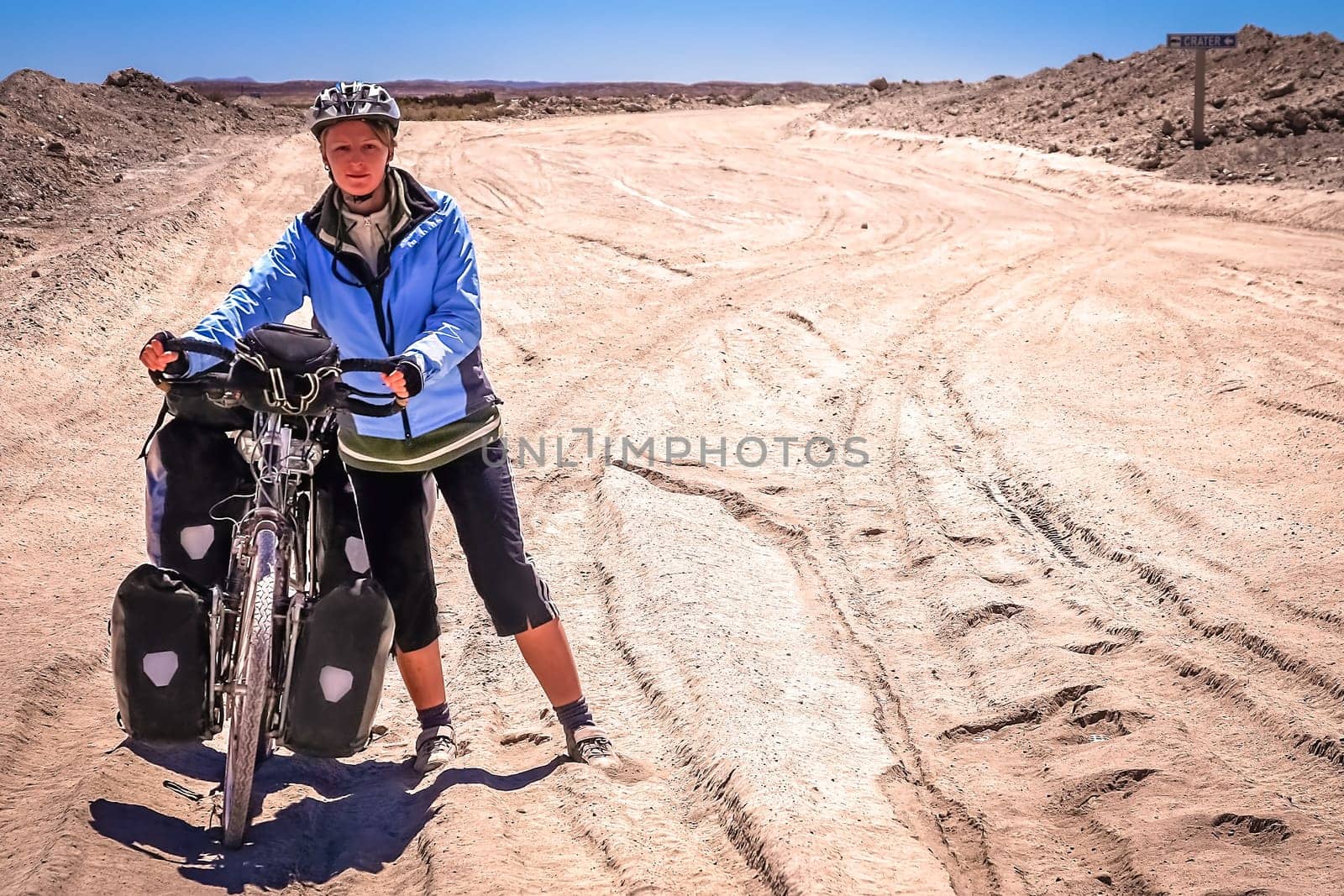 Woman cyclist struggling and pushing her bike on the sandy corrugated road in Altiplano in Bolivia