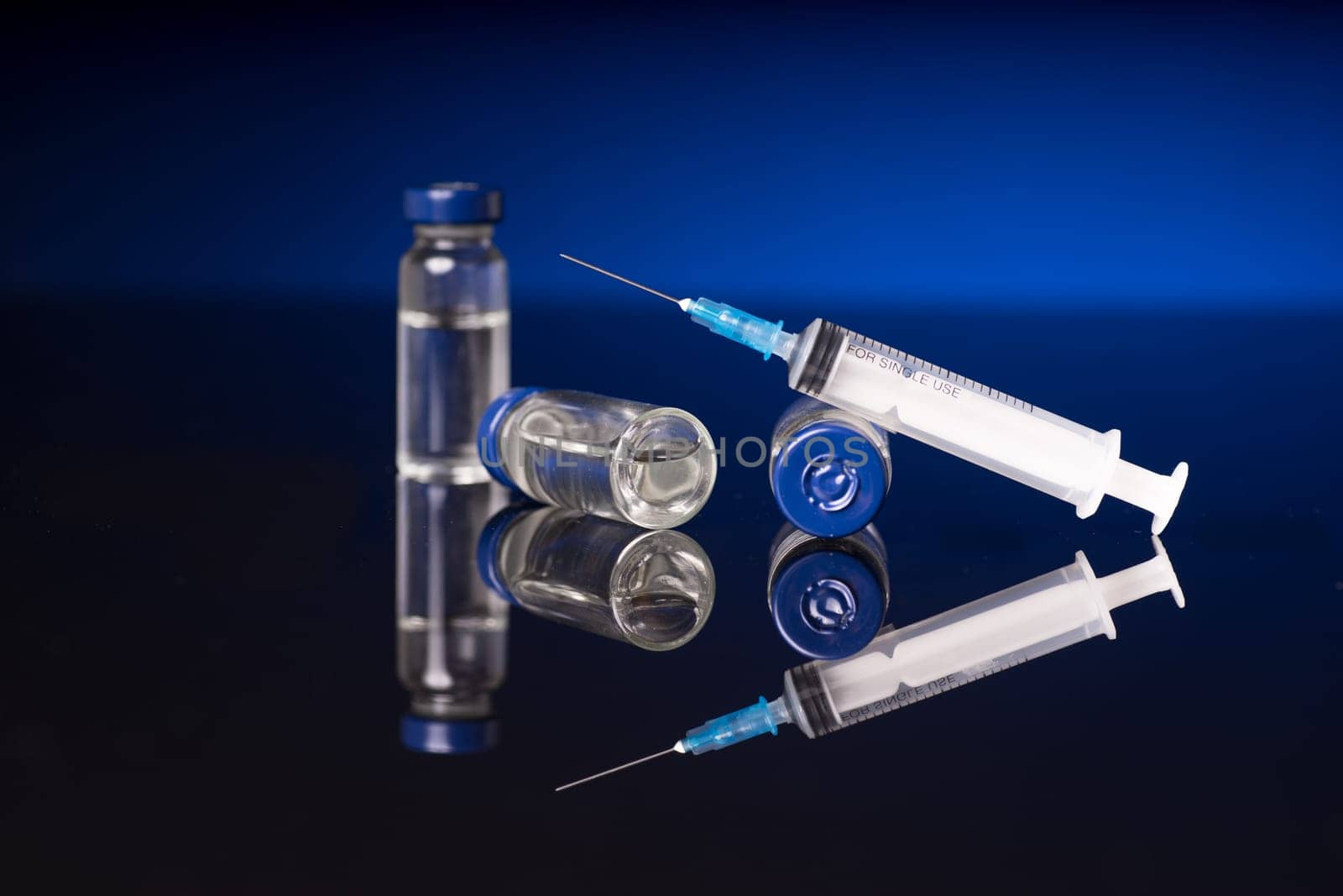 syringe and medical vials isolated on black blue background with glossy reflection