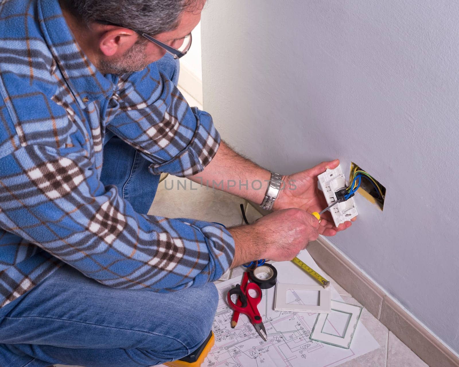The technician wears the normal protective devices. Electrician's hands assembles a standard bipolar wall socket.