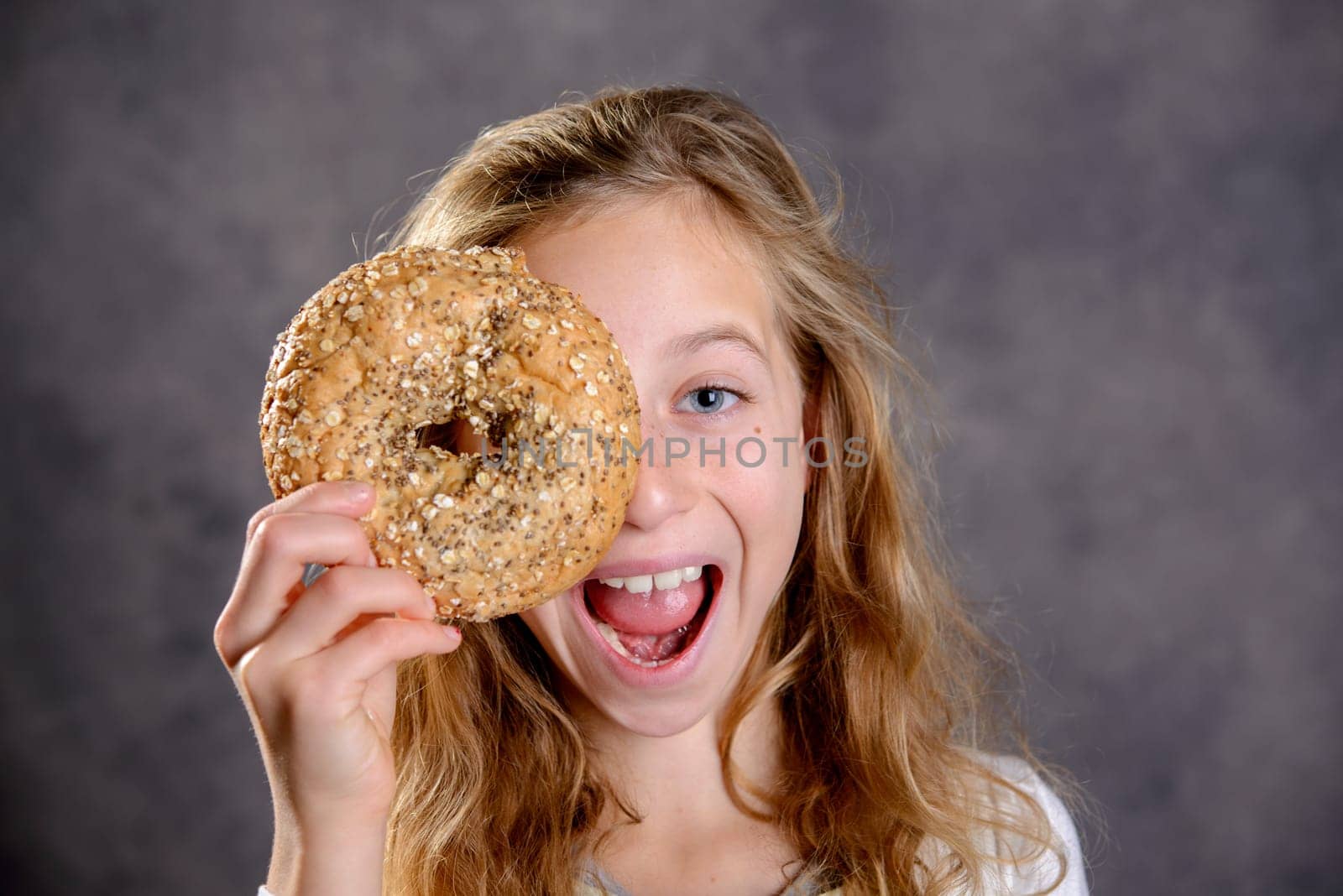nice blond girl in front of gray background looking through a big bagel