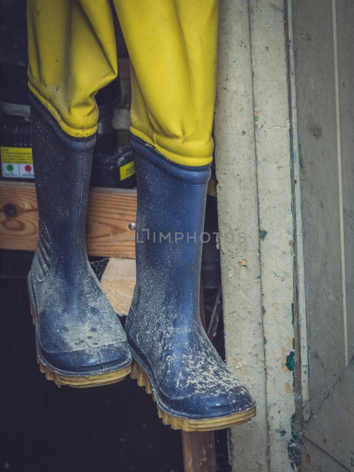 Dirty used rubber wellingtons hanging on a rack in a wooden shed in the garden