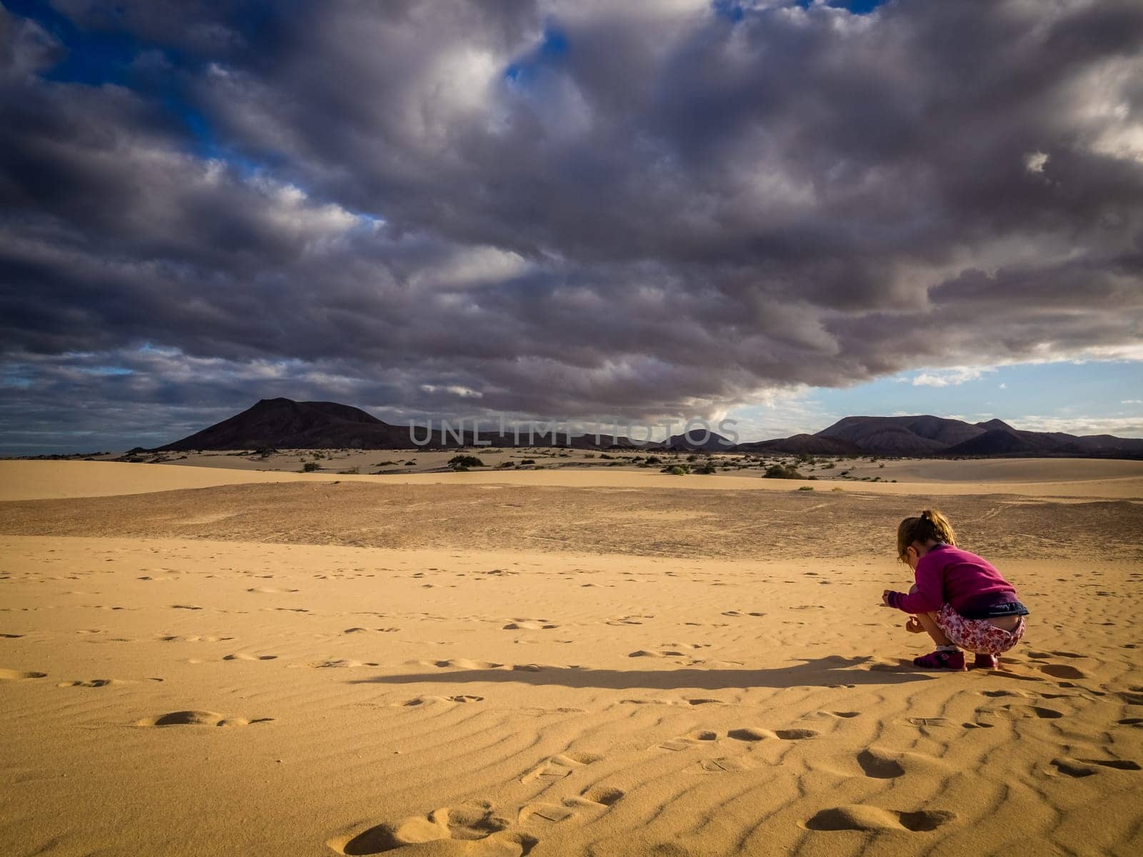 Little girl picking up small stones from the sand on the sand dunes in  the Natural Reserve of Dunes in Corralejo, fuerteventura, Canary Islands, Spain