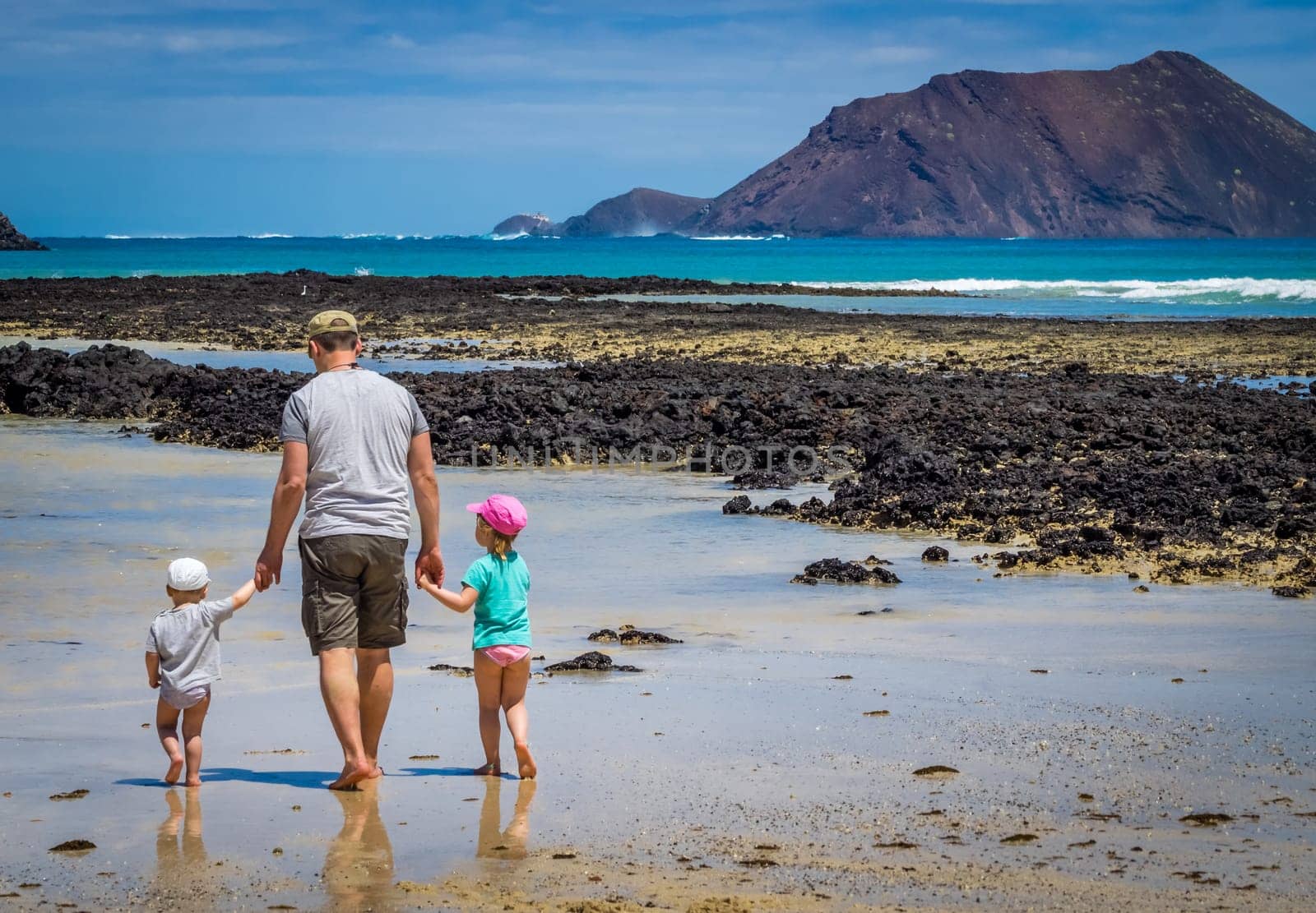 Father with his children, little boy and girl, walking in water waiting for wave to come on the beach in summer