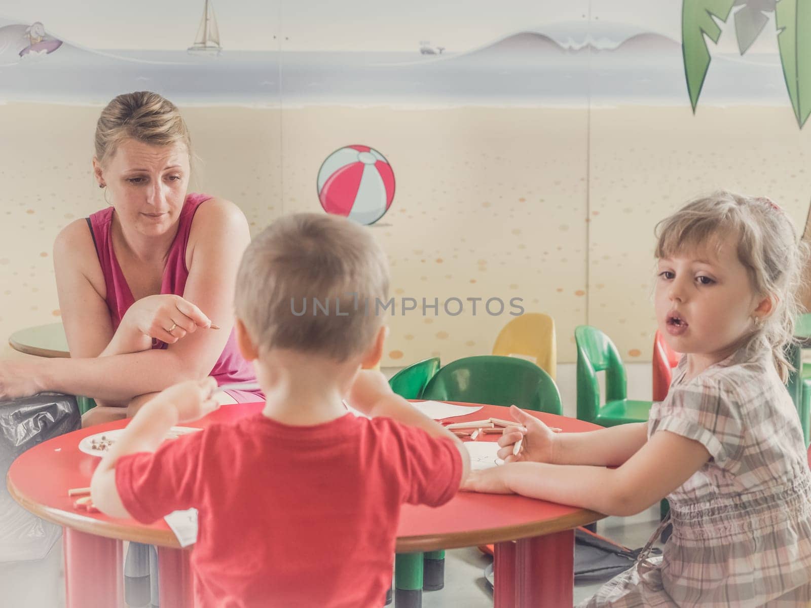 Woman and children drawing and coloring pictures during art time at the nursery