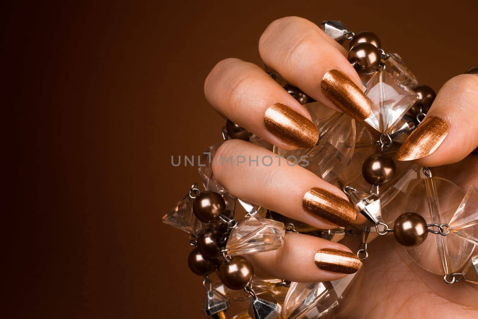 Female hand with glossy brown nails holds brown jewel from pearls.