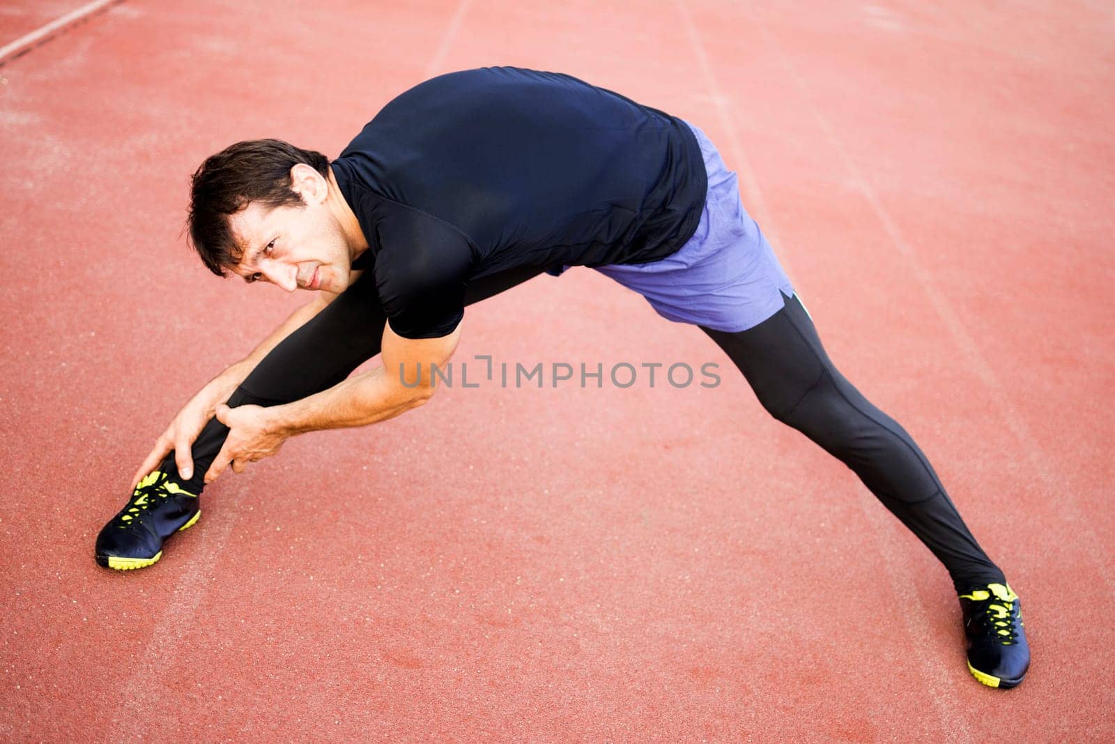 Man is exercising and stretching his legs in stadium outdoors.