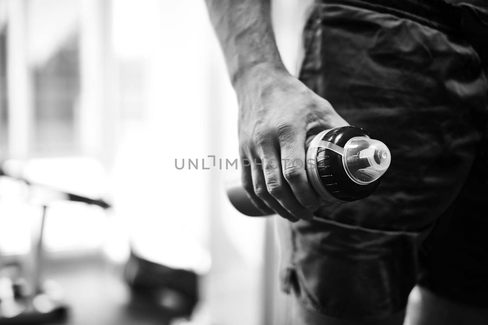 Hand of young man holding bottle with water in gym