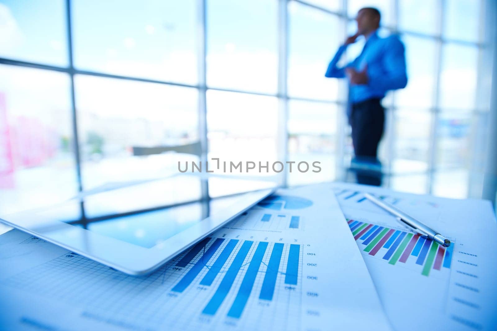 Digital tablet and financial documents on background of man calling