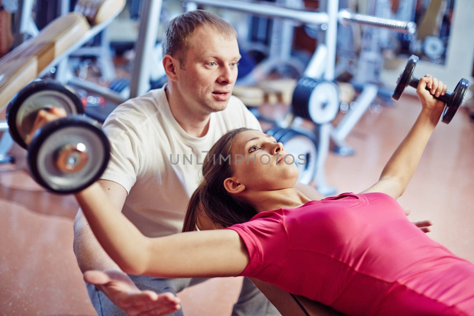 Portrait of pretty girl training in gym with her trainer helping her