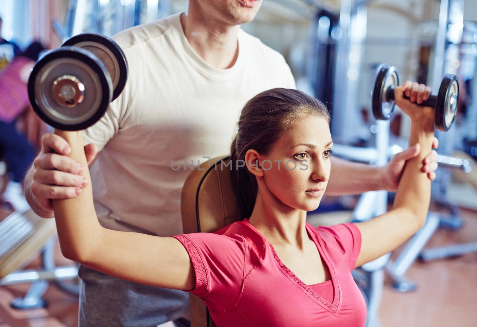Portrait of pretty girl training in gym with her trainer helping her