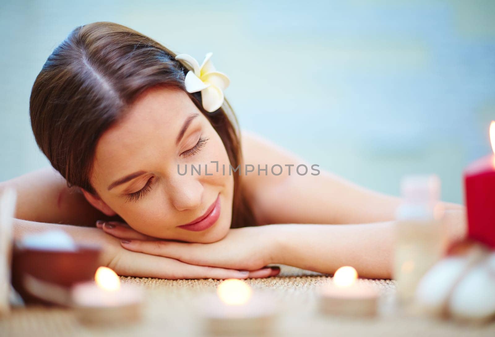 Relaxed female with frangipani flower in hair resting in spa salon