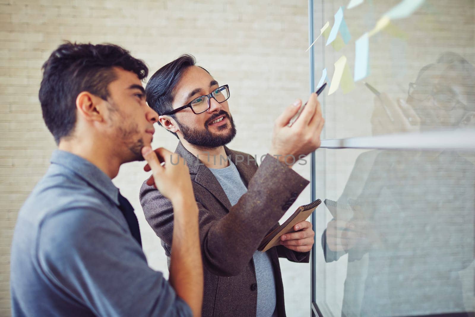 Asian manager pointing at reminder while talking to colleague in office