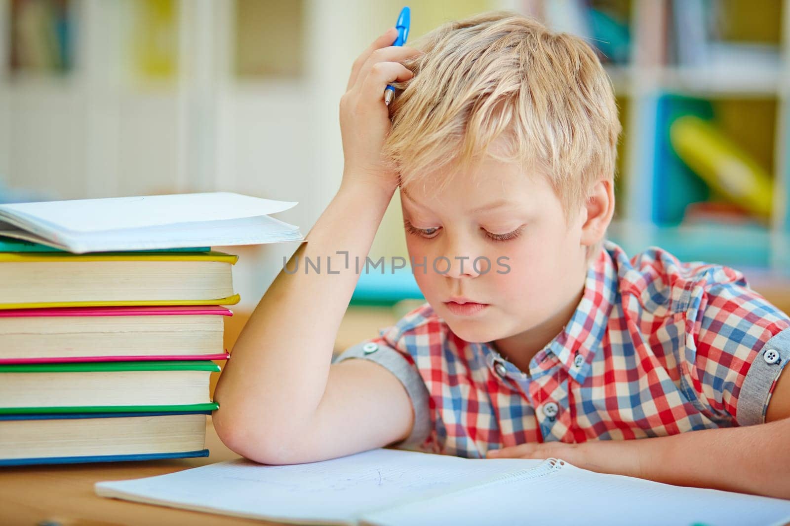 Pensive little boy looking at page of his copybook at lesson