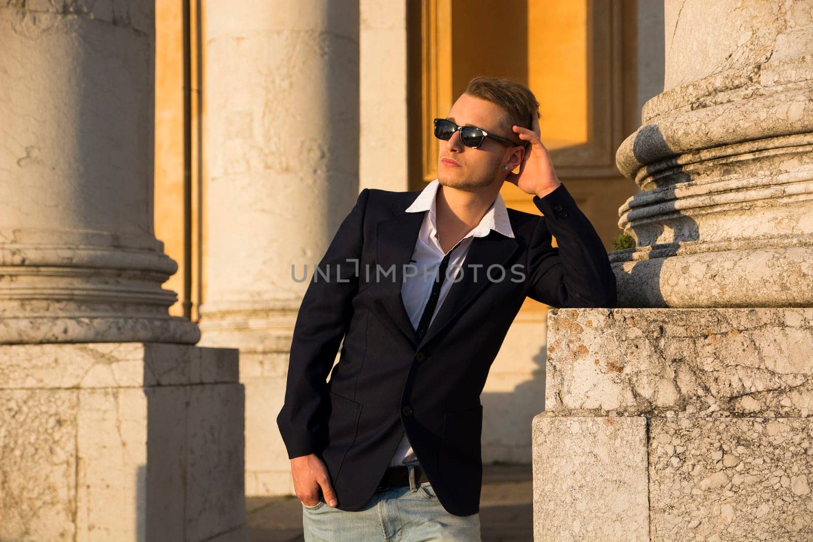Handsome blond young man with marble columns behind him, looking away
